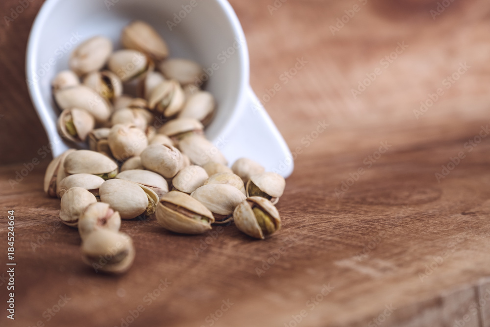 Closeup image of pistachios in a white cup on wooden background
