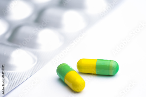 Green and yellow capsules on white background. Two medication pills with foil pack. photo