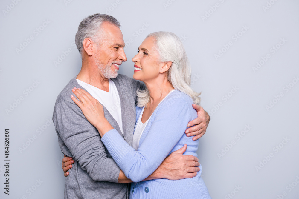 Portrait of lovely adorable cute happy senior couple, they are hugging, smiling and looking at each other, isolated on grey background - obrazy, fototapety, plakaty 