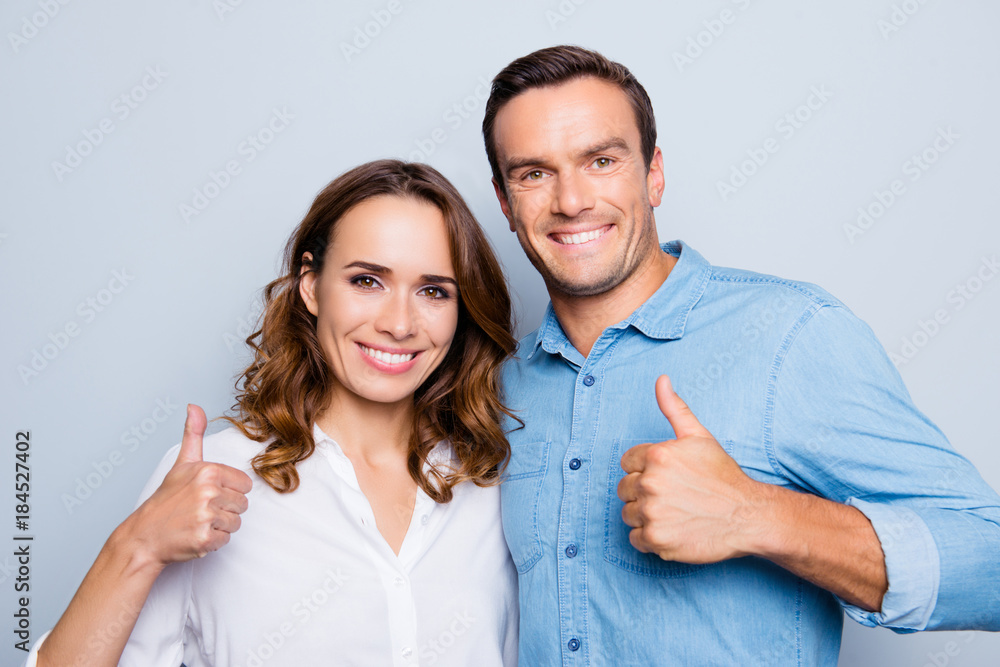 Closeup portrait of smiling couple gesturing thumbs up standing over grey background Closeup portrait of smiling couple gesturing thumbs up standing over grey background