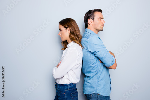 Portrait of unhappy frustrated couple standing back to back not speaking to each other after an argument while standing on grey background. Negative emotion face expression reaction