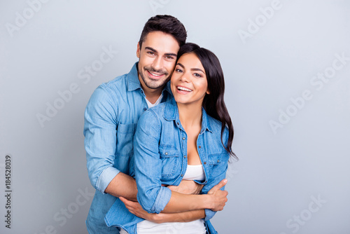 Portrait of cheerful lovely cute couple with beaming smiles hugging and looking at camera over grey background photo