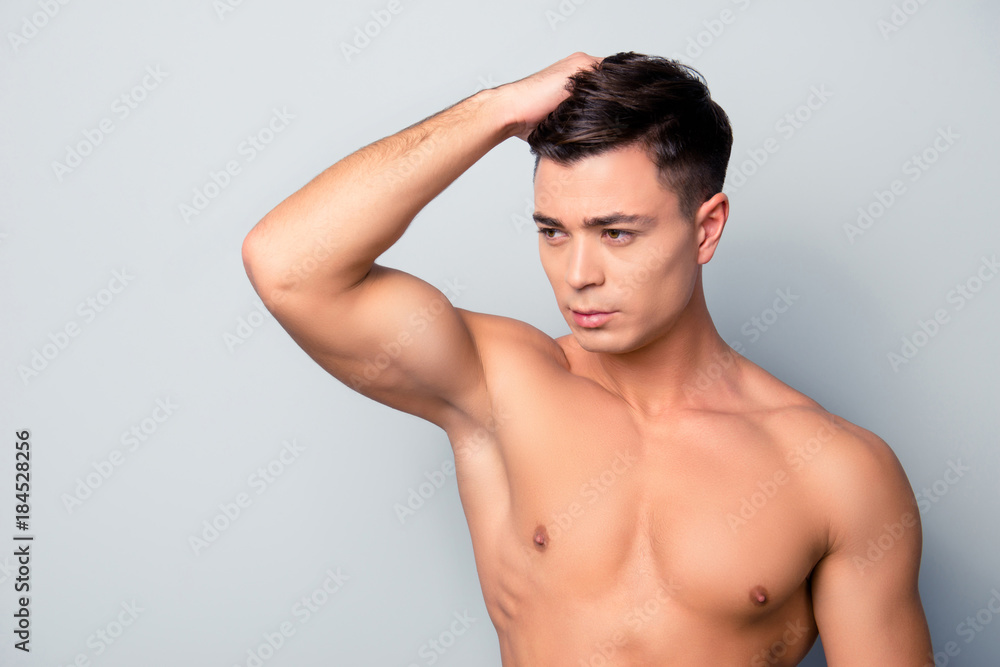Portrait of sexy confident serious handsome shaven with soft smooth flawless skin sportive man, he is combing his clear hairdress with a hand and applying balm, isolated on grey background, copy-space Portrait of sexy confident serious handsome shaven with soft smooth flawless skin sportive man, he is combing his clear hairdress with a hand and applying balm, isolated on grey background, copy-space