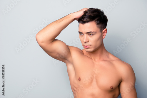 Portrait of sexy confident serious handsome shaven with soft smooth flawless skin sportive man, he is combing his clear hairdress with a hand and applying balm, isolated on grey background, copy-space