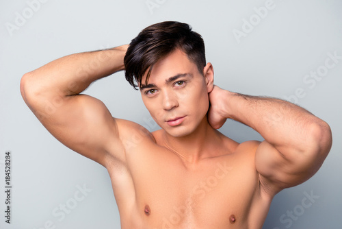 Close up portrait of confident sexy handsome muscular guy touching his clean brown hair and applying lotion and mask, isolated on grey background
