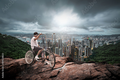 Man with bycicle up to the hill far from a vetical city