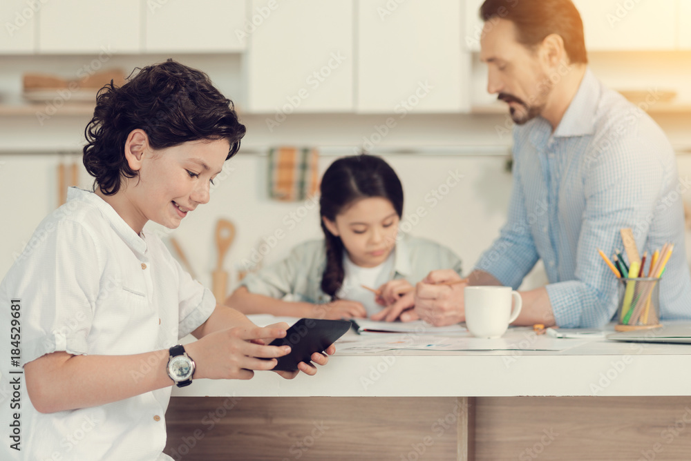 Digital games. Cheerful positive nice boy holding a tablet and playing on it while being at home Digital games. Cheerful positive nice boy holding a tablet and playing on it while being at home