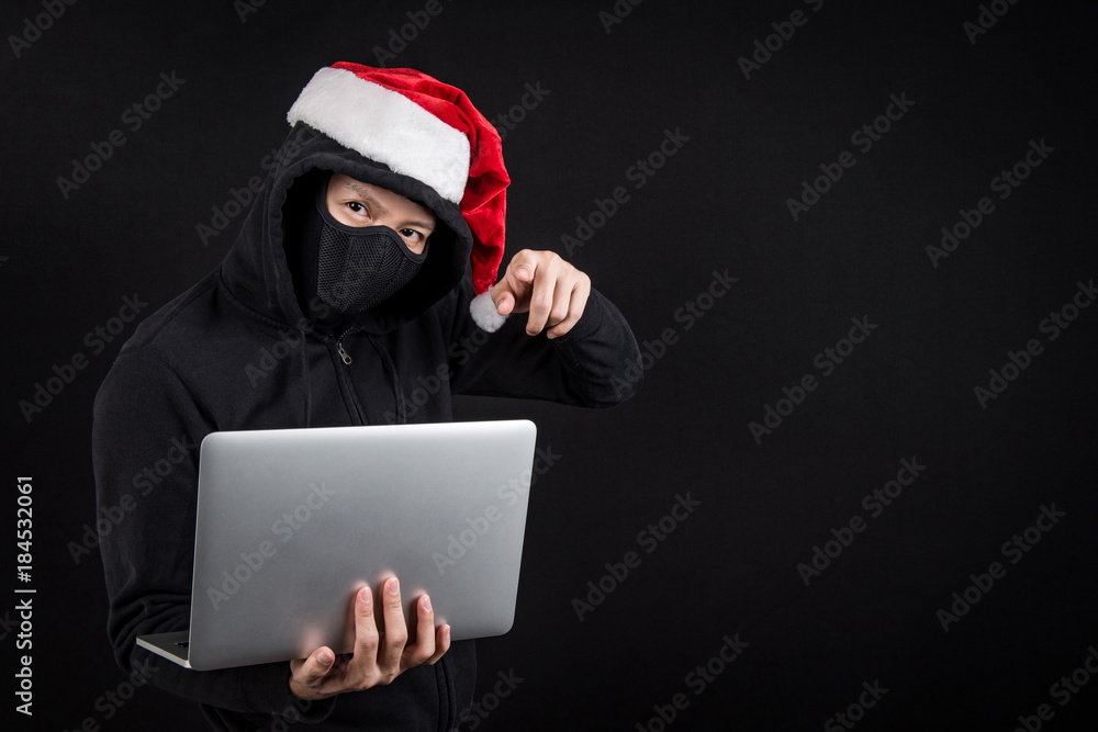 Mysterious male santa hacker holding laptop computer, anonymous man on black background, ransomware cyber attack and internet security on Christmas holiday concepts Mysterious male santa hacker holding laptop computer, anonymous man on black background, ransomware cyber attack and internet security on Christmas holiday concepts