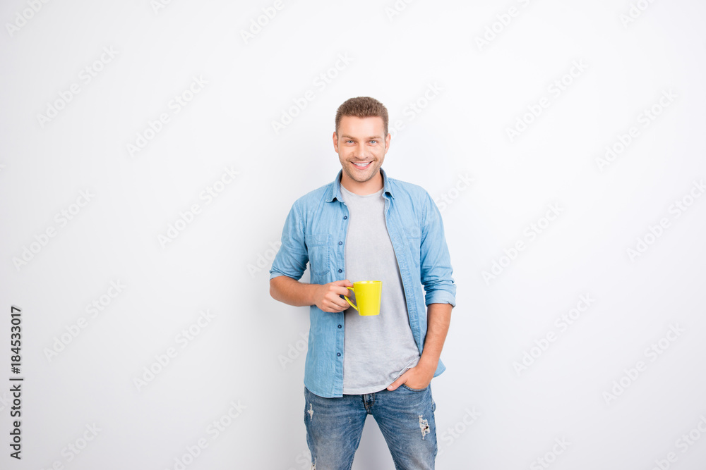 Portrait of cheerful, peppy guy holding yellow mug with coffee and one hand in pocket, getting a charge of vivacity, looking at camera, standing over white background Portrait of cheerful, peppy guy holding yellow mug with coffee and one hand in pocket, getting a charge of vivacity, looking at camera, standing over white background