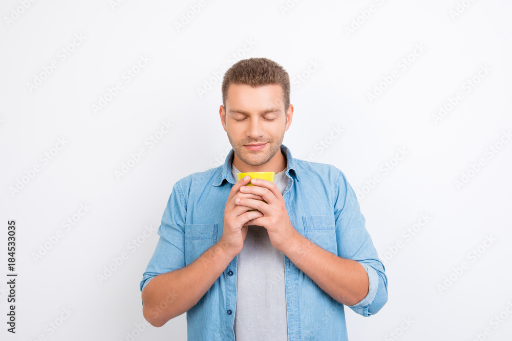 Portrait of handsome freelancer holding a cup of coffee with two hands, closed eyes, enjoying smell of coffee, morning ritual over white background Portrait of handsome freelancer holding a cup of coffee with two hands, closed eyes, enjoying smell of coffee, morning ritual over white background
