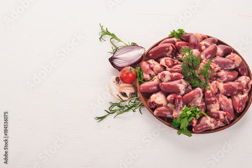 Raw chicken hearts on the plate ready for cooking with rosemary and spices on a white wooden background. Top view. Free space for text.