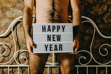 .Sexy Christmas image of a beautiful young man standing on his bed partialy naked celebrating new year. Lifestyle.