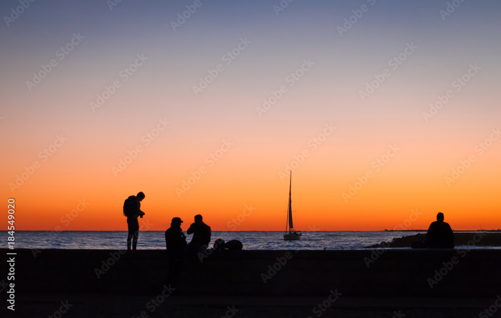 Silhouettes of several people and yacht with a big sail on the seaat the night
