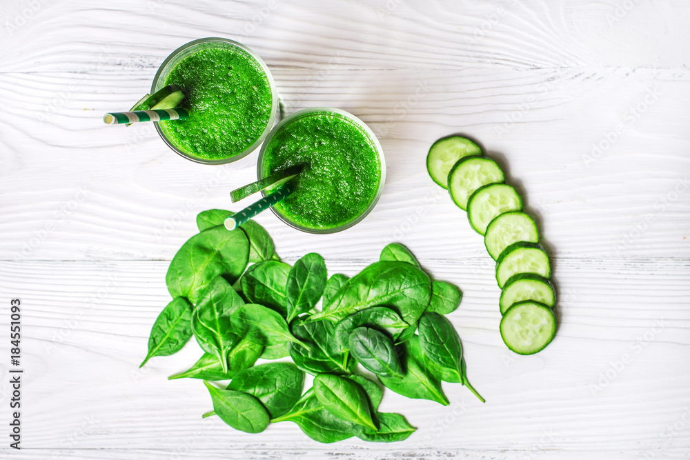 Obraz premium Green spinach and cucumber smoothie with ingredients on a white wooden background