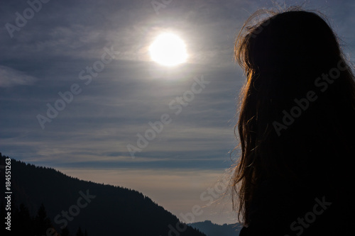 Girl looking at the sun.Valley and mountains in the background