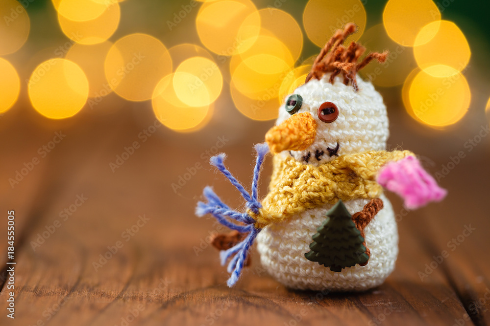 Obraz premium Handmade knitted snowman toy on wooden background with bokeh