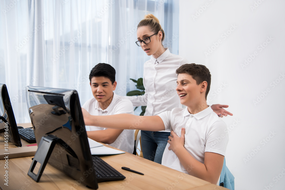 student pointing on screen to his classmates and laughing student pointing on screen to his classmates and laughing
