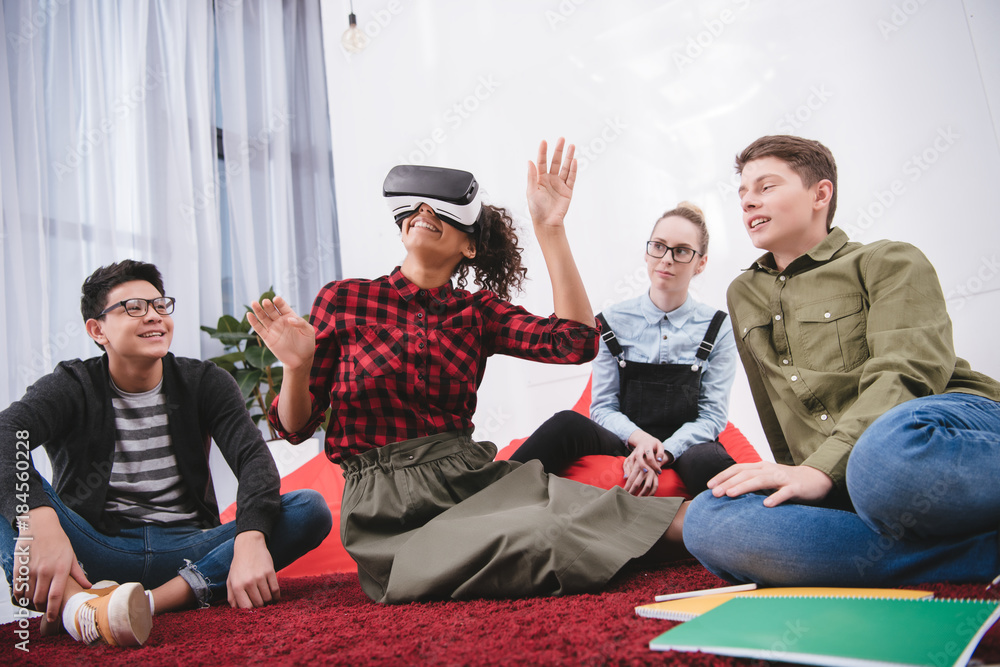 Fototapeta premium young girl in virtual reality glasses sitting on carpet with friends