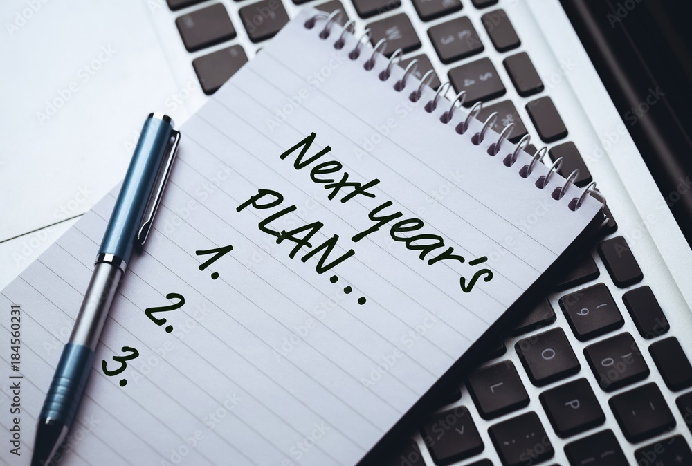 Top View of new years resolution written on notepad with pen on side laying on laptops keyboard Top View of new years resolution written on notepad with pen on side laying on laptops keyboard