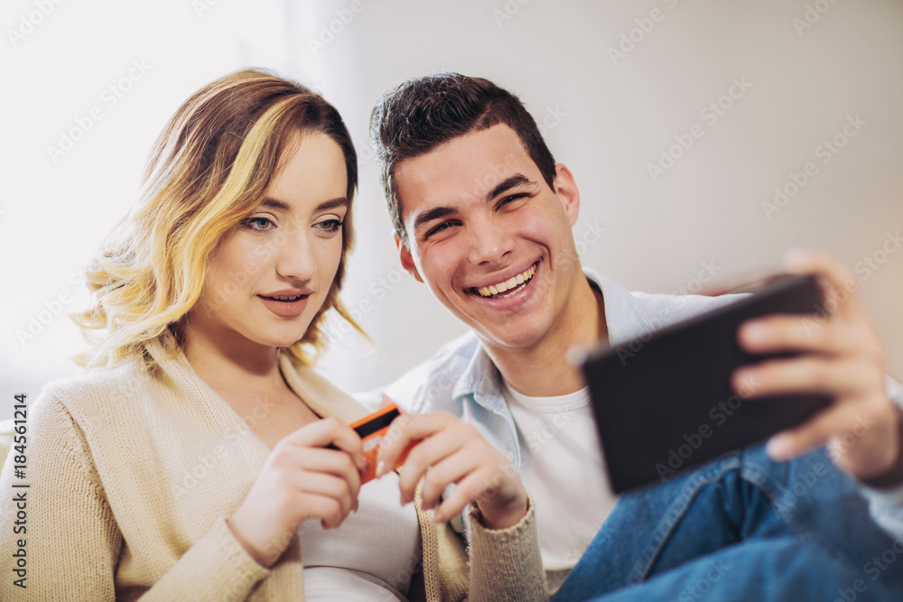 Young couple sitting on sofa and doing online shopping with tablet and credit card in room Young couple sitting on sofa and doing online shopping with tablet and credit card in room