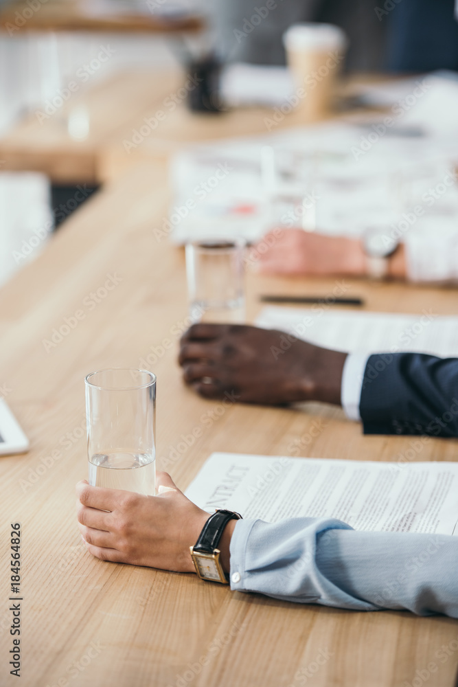 cropped shot of businesspeople sitting with glasses of water in conference hall cropped shot of businesspeople sitting with glasses of water in conference hall