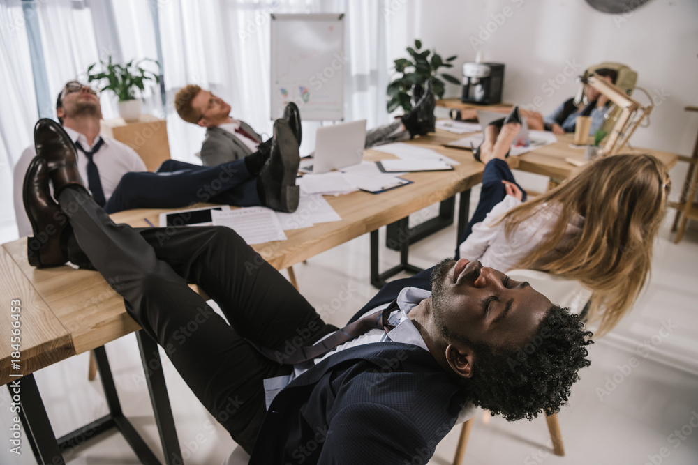 exhausted businesspeople sleeping in conference hall with feet on table exhausted businesspeople sleeping in conference hall with feet on table