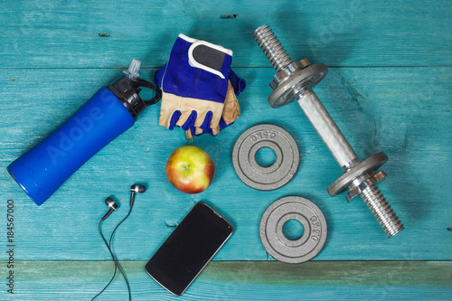 Weight plates, gloves and smartphone on wooden background