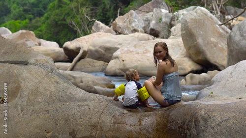 Mother and son sitting on a river with large stones in tropics photo