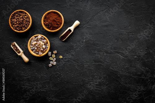 Coffee background. Roasted beans, ground coffee and sugar in bowls and scoops on black table top view copyspace