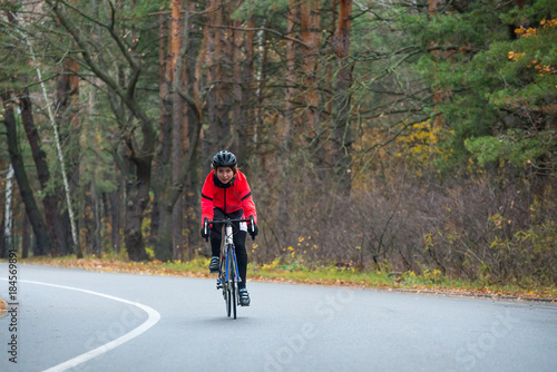 Young Woman in Orange Jacket Riding Road Bicycle in the Park in the Cold Autumn Day. Healthy Lifestyle.