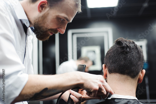 Master cuts hair and beard of men in the barbershop, hairdresser makes hairstyle for a young man