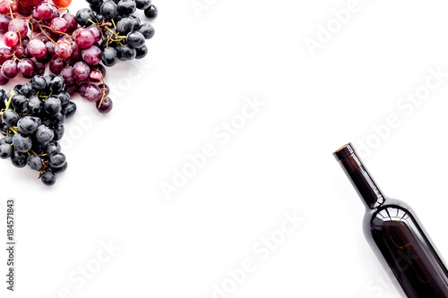 Wine bottle near bunches of red and black grapes on white background top view copyspace