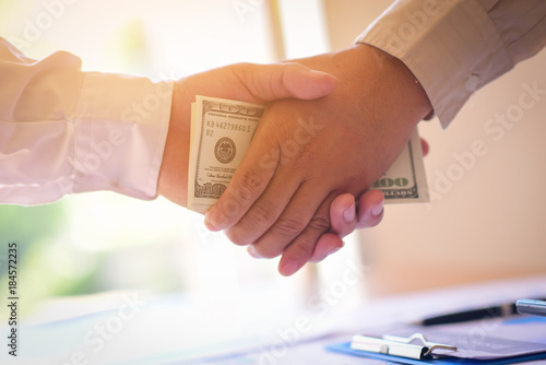 Businessmen making handshake with money in hands - bribery and corruption concepts photo