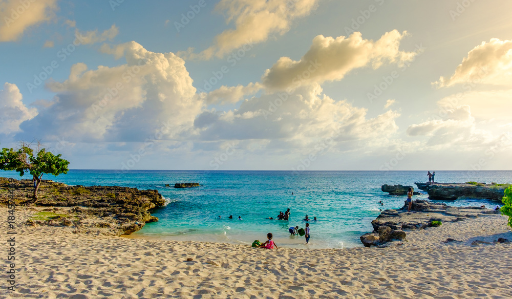 Fototapeta premium Grand Cayman, Cayman Islands, Smith's Barcadere beach in the Caribbean at sunset and people in the water