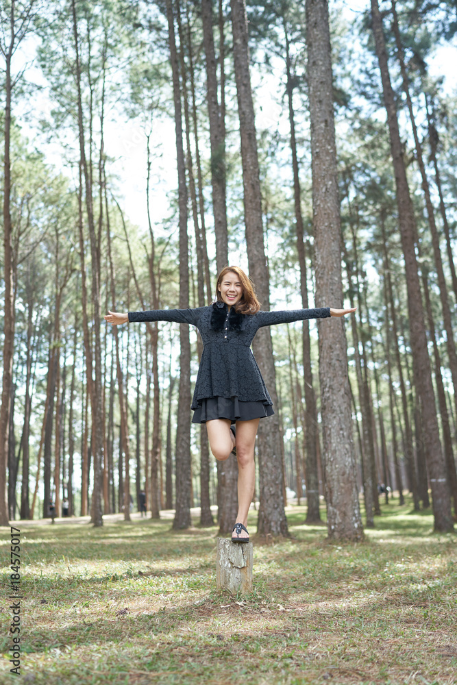 Beautiful asia woman with brown hair standing on one leg on stump in pine park