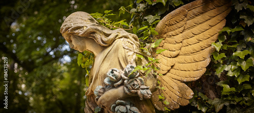 A fragment of ancient sculpture angel in a golden glow in the old cemetery.