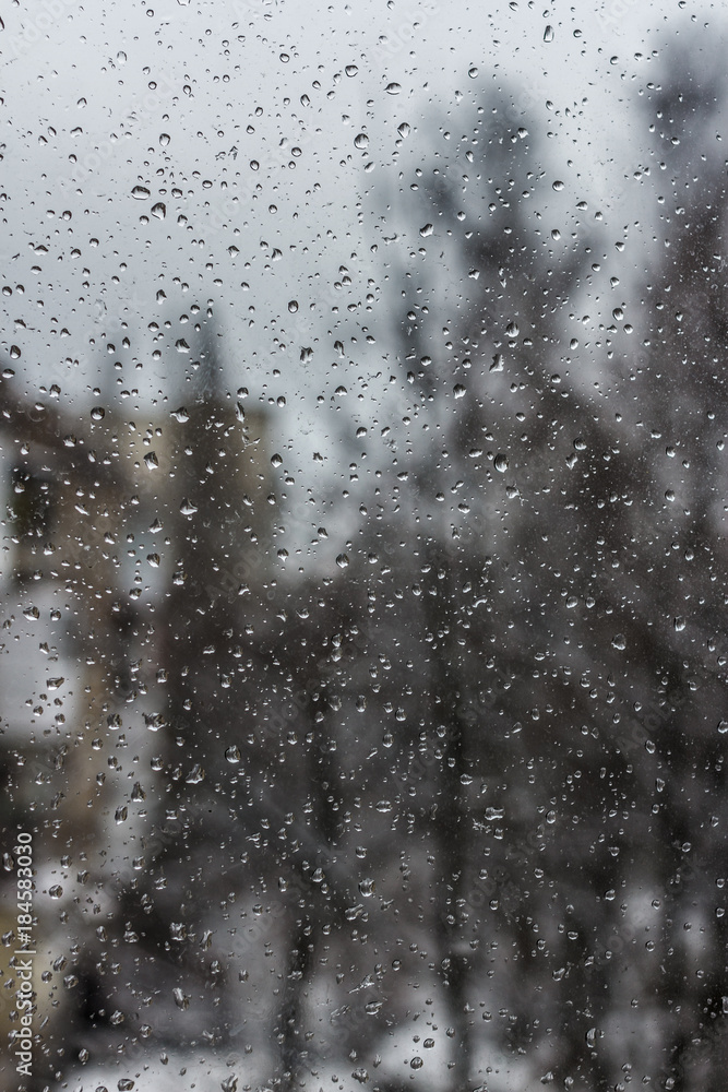 Raindrops on window with tree background. Snow and rain weather. Bubble background. Rain drops on a glass.