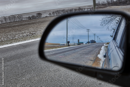 Rural road in farmland seen through rear view mirror