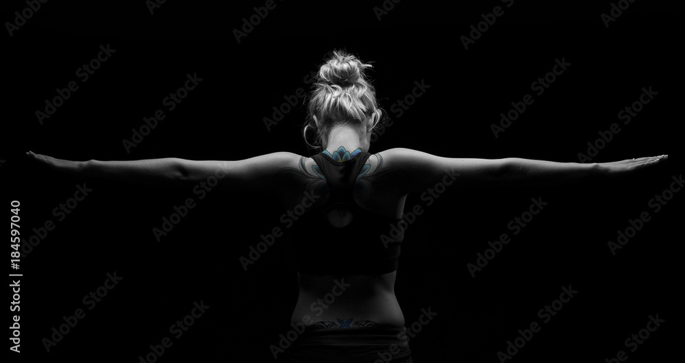 Beautiful fit and healthy blond woman in black top in dark with arms stretched from behind artistic conversion Beautiful fit and healthy blond woman in black top in dark with arms stretched from behind artistic conversion
