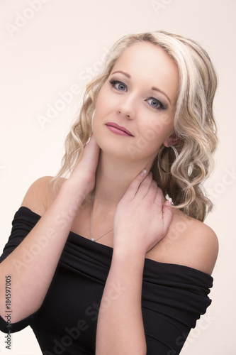 Beautiful blond woman in curly hair and black top on light background