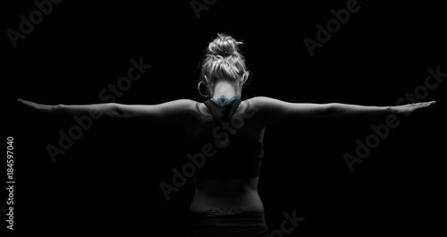 Beautiful fit and healthy blond woman in black top in dark with arms stretched from behind artistic conversion