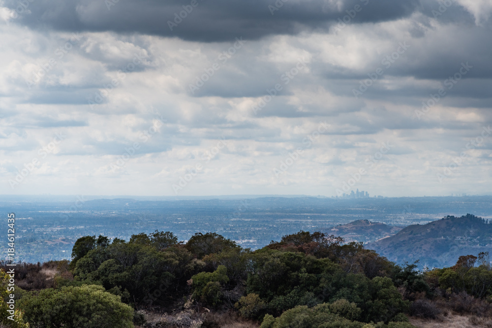 A view of the Los Angeles skyline from distant mountains with dark clouds hanging above.