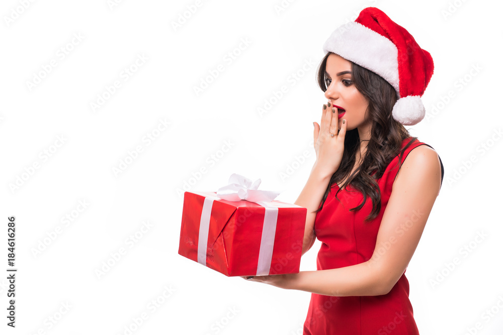 Shocked young woman in red dress wearing christmas hat standing isolated over white wall background. Looking camera holding gift box surprise. Shocked young woman in red dress wearing christmas hat standing isolated over white wall background. Looking camera holding gift box surprise.