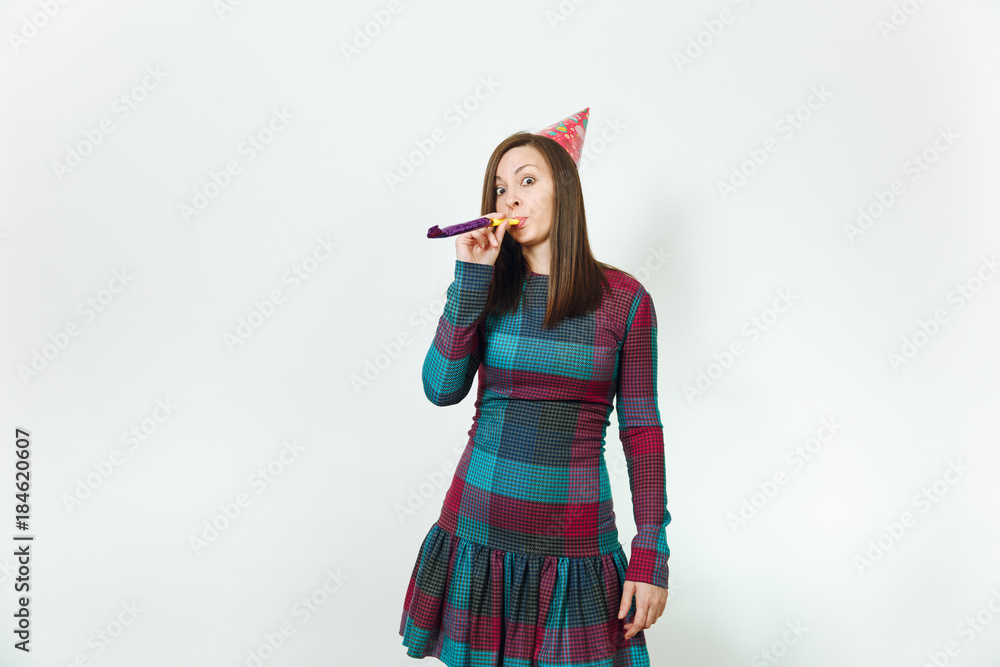 Beautiful caucasian fun young happy woman in plaid dress and birthday party hat with shy charming smile, playing pipe, celebrating and enjoying holiday on white background isolated for advertisement. Beautiful caucasian fun young happy woman in plaid dress and birthday party hat with shy charming smile, playing pipe, celebrating and enjoying holiday on white background isolated for advertisement.