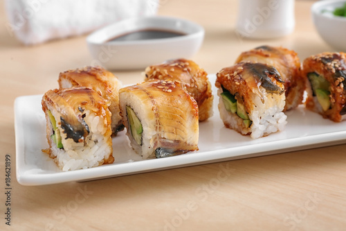 Plate with tasty sushi rolls on table, closeup