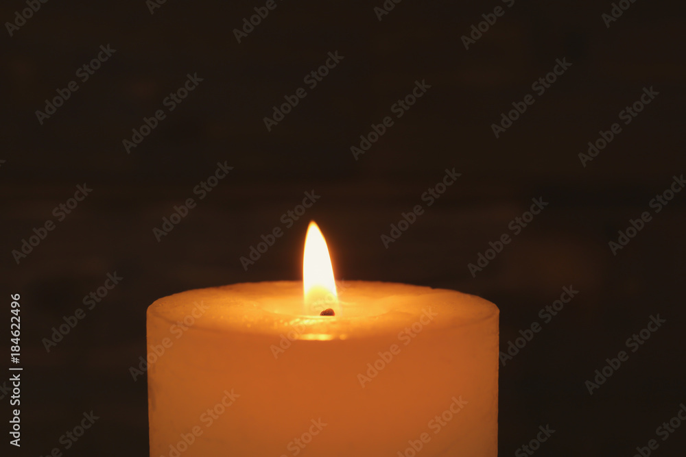 Wax candle burning on dark background, closeup Wax candle burning on dark background, closeup