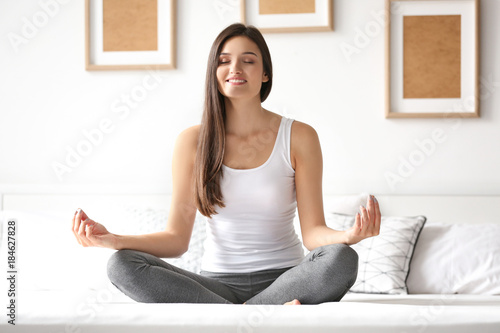 Young woman meditating in bed at home