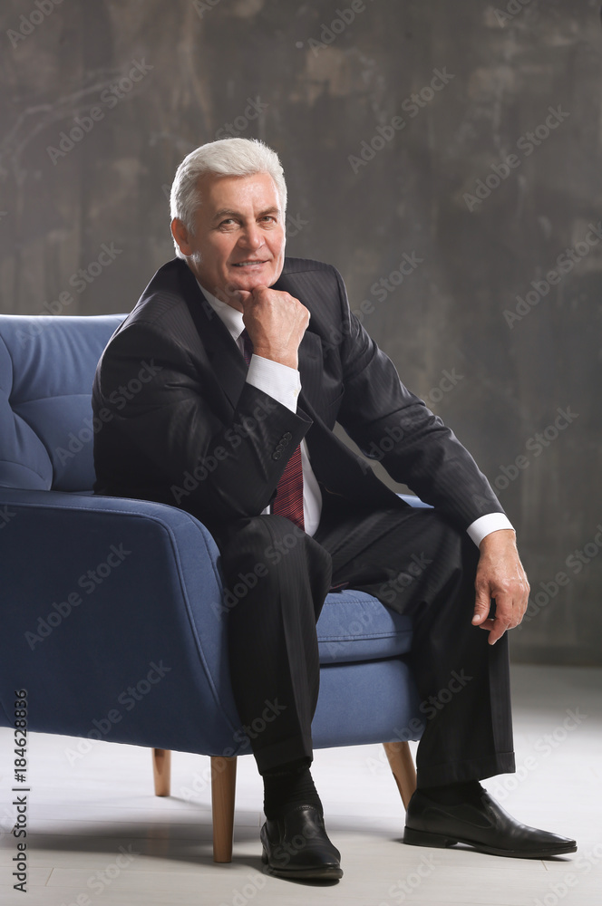 Handsome mature man sitting in armchair on dark background Handsome mature man sitting in armchair on dark background