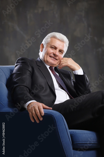 Handsome mature man sitting in armchair on dark background