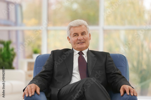 Handsome mature man sitting in armchair indoors